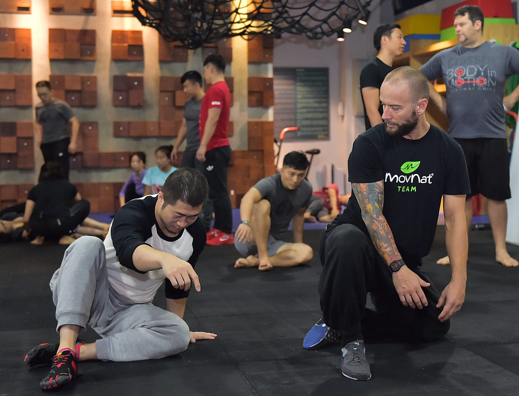 Authentic documentary photography of a certified natural movement coach guiding an adult student on balance and mindful movement outdoors on a fallen log or low balance beam in a sunlit park or natural training ground.