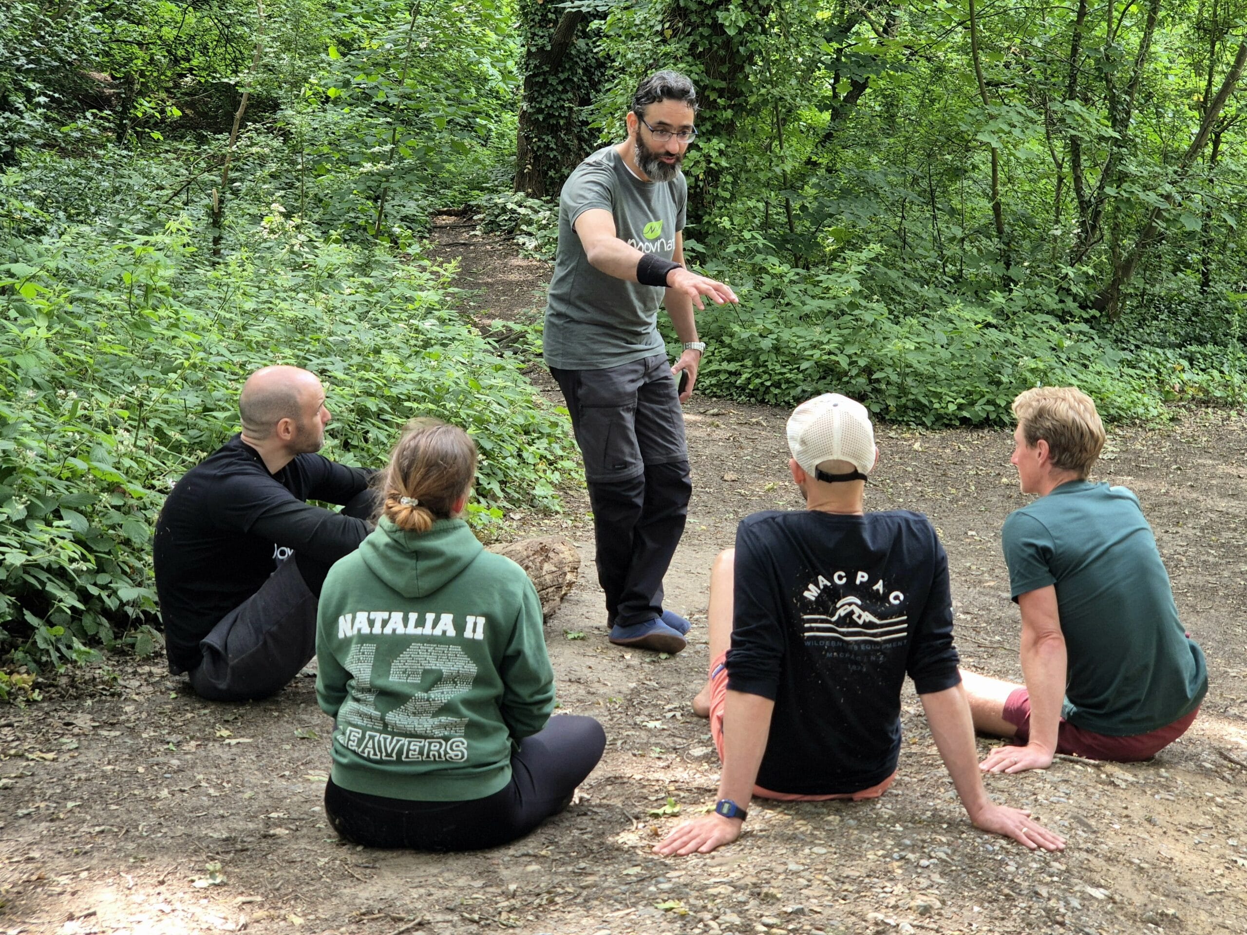 Documentary photography of an experienced movement mentor and a newly certified coach reviewing notes and discussing movement progressions at an outdoor wooden bench under trees with a notebook and coffee.