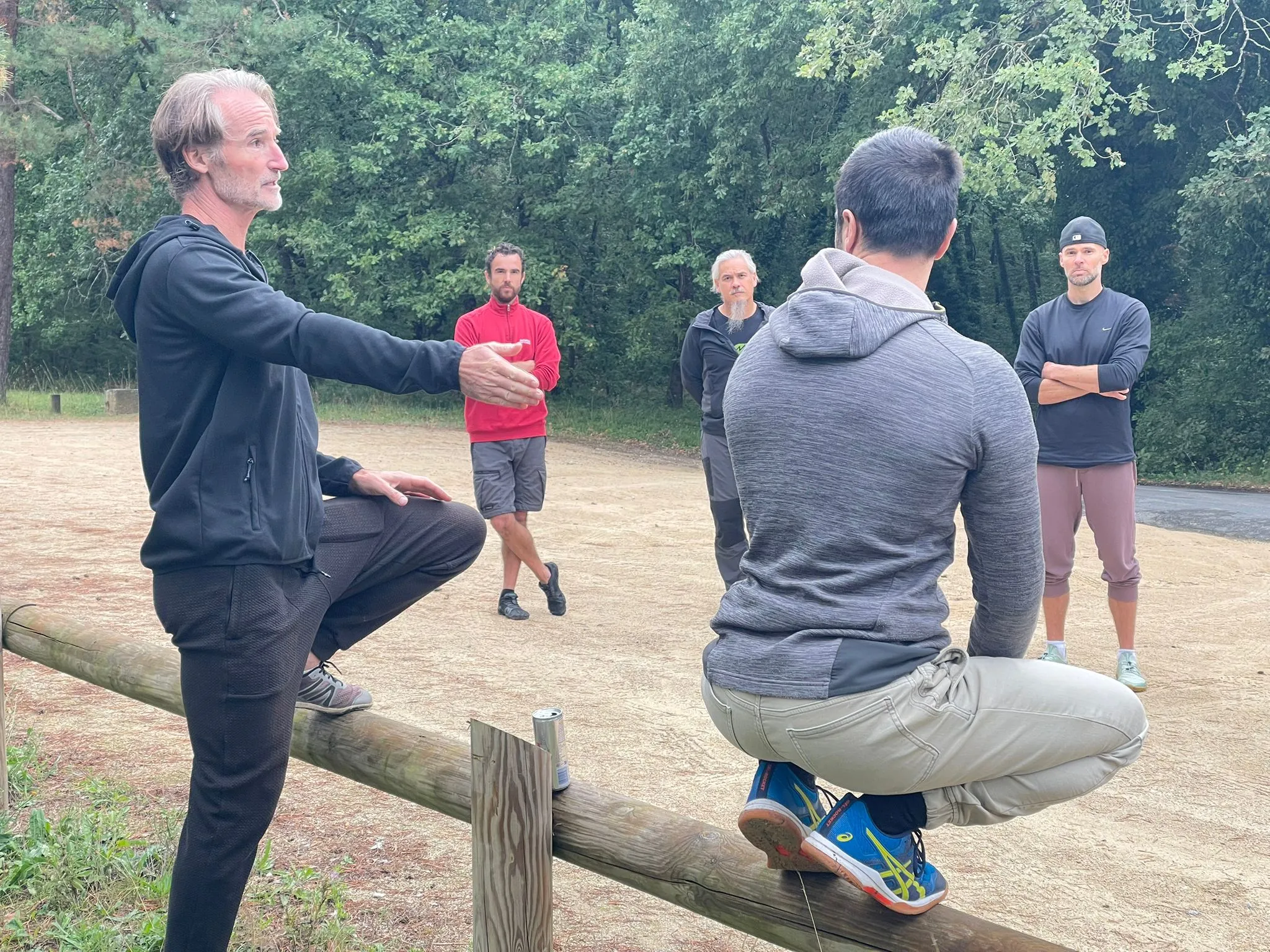 Documentary lifestyle photography of a natural movement coach instructing an adult client on floor work, ground-to-standing transition, kneeling to standing get-ups in an open wood-floor movement studio.
